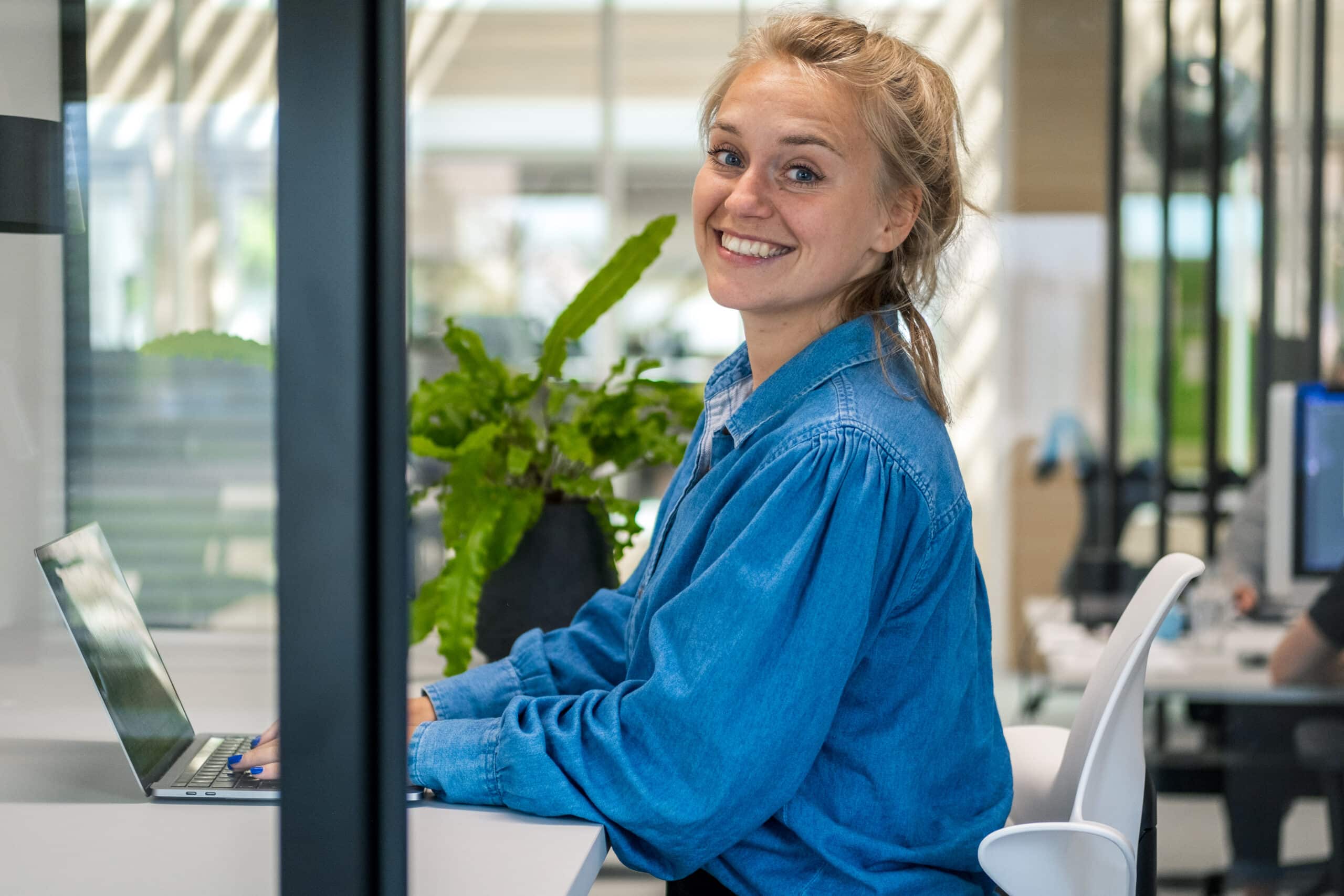 Lachende jonge vrouw zittend aan een bureau in een modern kantoor